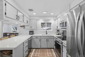 Kitchen with stainless steel appliances, light stone countertops, light wood finished floors, recessed lighting, and backsplash