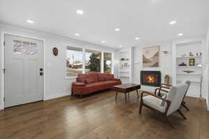 Living room with a fireplace, wood-type flooring, built in features, and recessed lighting