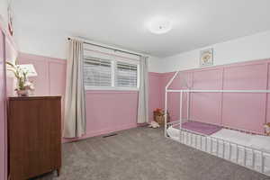 Unfurnished bedroom featuring a decorative wall, a wainscoted wall, and carpet