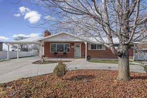 View of front of property featuring driveway, a porch, a carport, brick siding, and a chimney