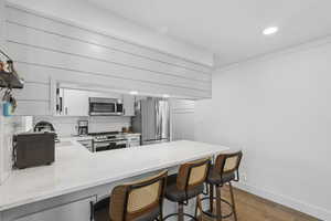 Kitchen featuring light stone counters, a peninsula, white cabinetry, a kitchen breakfast bar, and appliances with stainless steel finishes