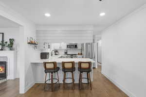 Kitchen featuring a breakfast bar area, ornamental molding, white cabinets, a brick fireplace, and backsplash