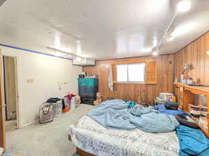 Bedroom featuring track lighting, wood walls, carpet, and a textured ceiling