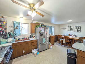 Kitchen with brown cabinets, light countertops, stainless steel appliances, light carpet, and a ceiling fan