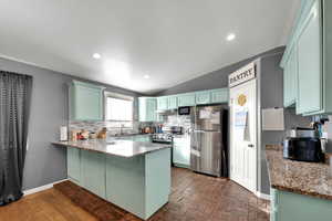 Kitchen with a peninsula, light stone counters, stainless steel appliances, brick patterned flooring, and backsplash