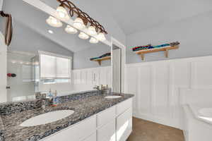 Full bath featuring a bath, double vanity, lofted ceiling, light tile patterned floors, and a shower stall
