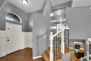 Entryway featuring a stone fireplace, dark wood finished floors, wainscoting, and stairs