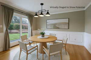 Dining space with a wainscoted wall, crown molding, light wood finished floors, and a decorative wall