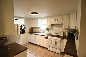 Kitchen featuring dark countertops, white appliances, white cabinetry, and under cabinet range hood