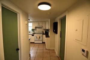 Kitchen featuring white electric stove, white cabinetry, light tile patterned flooring, electric panel, and dark countertops