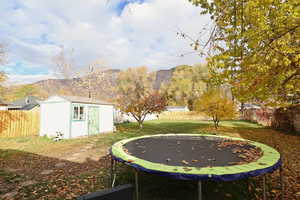 Fenced backyard featuring a trampoline, a shed, and a mountain view