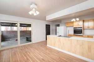 Kitchen with light countertops, stainless steel oven, light brown cabinets, light wood-style floors, and white refrigerator with ice dispenser