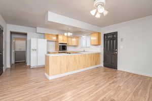 Kitchen featuring light countertops, white refrigerator with ice dispenser, light brown cabinets, a peninsula, and stainless steel oven