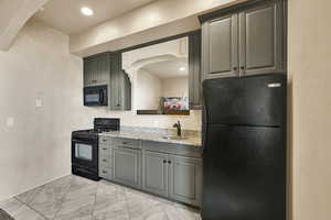 Kitchen with black appliances, light stone countertops, arched walkways, gray cabinetry, and recessed lighting