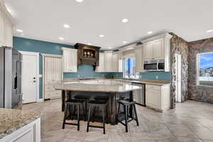 Kitchen with light stone countertops, stainless steel appliances, a kitchen bar, a kitchen island, and recessed lighting