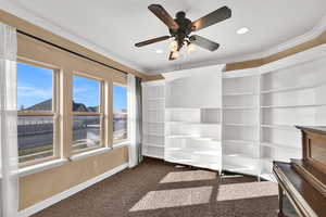 Interior space with ornamental molding, dark colored carpet, ceiling fan, and recessed lighting