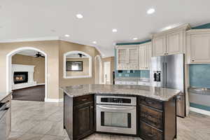 Kitchen featuring dark brown cabinets, arched walkways, glass insert cabinets, light stone countertops, and a kitchen island