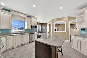 Kitchen with arched walkways, light stone counters, cream cabinets, ornamental molding, and recessed lighting