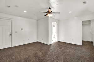 Unfurnished bedroom with recessed lighting, dark carpet, ceiling fan, arched walkways, and a spacious closet