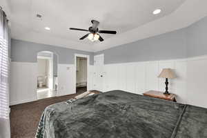 Carpeted bedroom with recessed lighting, arched walkways, a ceiling fan, wainscoting, and a raised ceiling