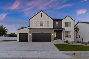 View of front of house with an attached garage, driveway, a standing seam roof, a metal roof, and stucco siding