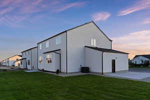 Back of property at dusk with a yard, stucco siding, and a patio area