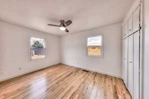 Unfurnished primary bedroom with a closet, hardwood floors, and ceiling fan