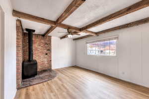 Den/office/bonus room with a wood stove, light wood finished floors, beam ceiling, a ceiling fan, and a textured ceiling
