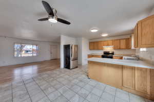 Kitchen with a peninsula, light countertops, freestanding refrigerator, black range with electric cooktop, and light tile patterned flooring