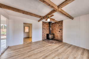 Den/office/bonus room with beamed ceiling, a wood stove, wood finished floors, a textured ceiling, and ceiling fan