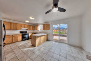 Kitchen featuring light countertops, black electric range, freestanding refrigerator, and a peninsula