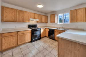 Kitchen featuring black appliances, light countertops, under cabinet range hood, light tile patterned floors, and brown cabinetry