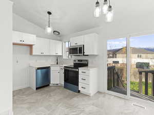 Kitchen featuring stainless steel appliances, decorative light fixtures, lofted ceiling, light countertops, and white cabinetry