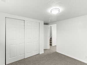 Unfurnished bedroom featuring a textured ceiling, a closet, and carpet flooring