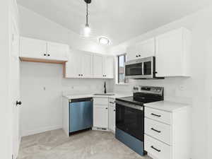 Kitchen with appliances with stainless steel finishes, white cabinetry, light countertops, vaulted ceiling, and pendant lighting