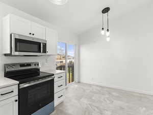 Kitchen with appliances with stainless steel finishes, white cabinetry, hanging light fixtures, and light marble finish flooring