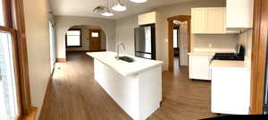 Kitchen with arched walkways, open flow island, white cabinetry, light countertops, black gas stove, and freestanding refrigerator, dishwasher and microwave.