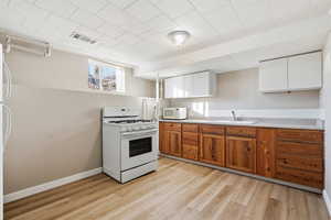 MIL - Kitchen with brown cabinetry, white appliances, white cabinets, light countertops, and light wood-style floors