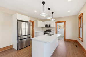 Kitchen with appliances with stainless steel finishes, white cabinets, pendant lighting, light wood-style floors, and recessed lighting