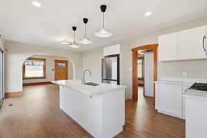 Kitchen with white cabinetry, arched walkways, a center island with sink, stainless steel appliances, and light wood finished floors