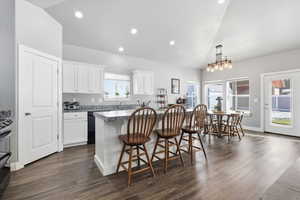 Kitchen featuring a breakfast bar, a kitchen island, lofted ceiling, white cabinetry, and dark wood-style floors