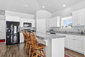 Kitchen featuring black appliances, white cabinets, light stone countertops, a center island, and a breakfast bar area