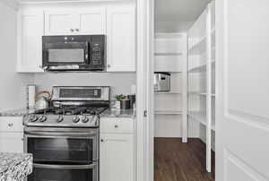 Kitchen featuring range with two ovens, white cabinetry, black microwave, and light stone counters