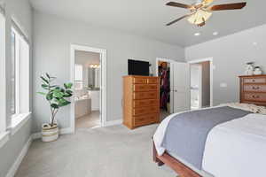 Primary Bedroom featuring connected bathroom, light carpet, ceiling fan, and a spacious closet