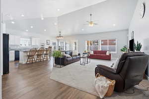 Living area with lofted ceiling, dark wood finished floors, a ceiling fan, a chandelier, and healthy amount of natural light