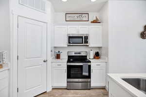 Kitchen with appliances with stainless steel finishes, white cabinetry, light wood-style flooring, and recessed lighting