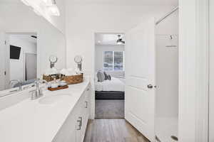 Ensuite bathroom featuring vanity, shower, light wood-style floors, and a ceiling fan
