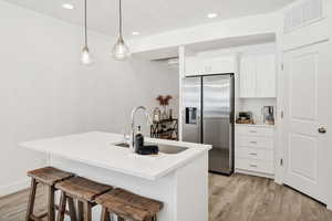 Kitchen featuring stainless steel refrigerator with ice dispenser, a kitchen bar, hanging light fixtures, light wood-type flooring, and white cabinetry
