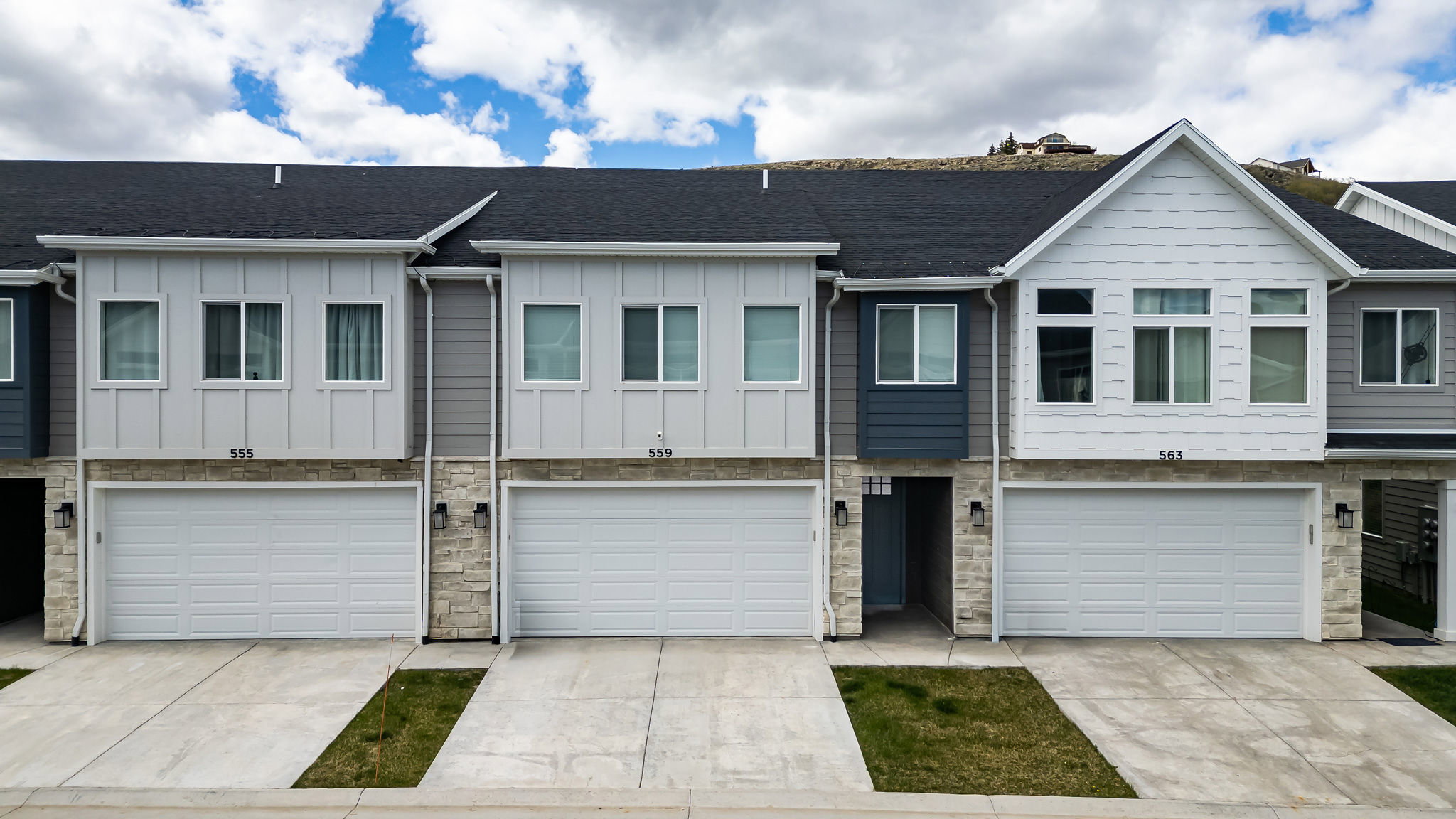 View of front of home featuring board and batten siding, an attached garage, stone siding, driveway, and a shingled roof