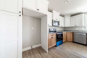 Kitchen with appliances with stainless steel finishes, white cabinets, light stone countertops, light wood-style floors, and brown cabinets